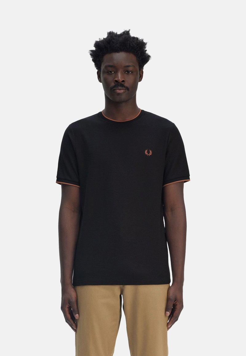 Camiseta de algodón negra de manga corta con ribete naranja, que presenta un pequeño logo bordado en el lado izquierdo del pecho. Diseño de ajuste casual y cuello redondo.