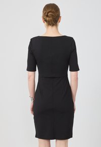 Robe noire cintrée avec des manches courtes, un col dégagé et des coutures structurées. Tissu lisse avec un ourlet au genou. Pas de motifs ni d'accents visibles.