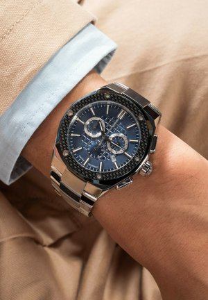 Silberne Edelstahl-Armbanduhr mit einem dunkelblauen gemusterten Zifferblatt, Chronograph-Funktionen und schwarzen Carbonfaser-Akzenten.
