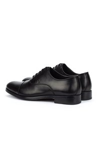 Par de zapatos de vestir Oxford de cuero negro con cordones cerrados, tacón bajo apilado y detalle de puntera, vistos de lado sobre un fondo blanco.