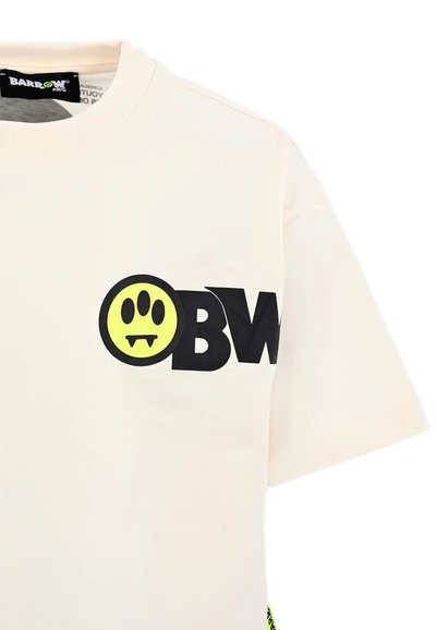 T-shirt w kolorze kremowym z bawełny, z wyraźnym czarnym napisem "OBW" oraz żółtą okrągłą grafiką z twarzą, krótkie rękawy i okrągły dekolt.