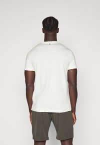 Tricou alb cu mânecă scurtă, guler rotund, material texturat și un mic detaliu verde pe spate. Asortat cu pantaloni scurți de culoare verde oliv.