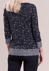 Top nero con un motivo di stelle bianche, maniche 3/4 e orlo a stampa floreale solida. Tessuto morbido con una texture liscia e una vestibilità comoda.