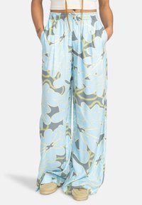 Pantalons larges bleu clair en tissu lisse, ornés de grands motifs floraux gris et vert citron, avec une taille élastique et des poches.