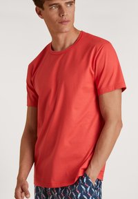Rode T-shirt met korte mouwen, gemaakt van zacht materiaal, met een ronde hals en een gladde textuur, gecombineerd met blauw met patroon shorts.