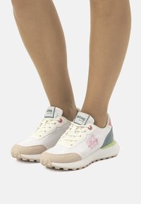 Zapatillas deportivas blancas con acentos en tonos pastel, que cuentan con una puntera texturizada, parte delantera con cordones y detalle de logo en el lateral. Suela de goma para mayor tracción.