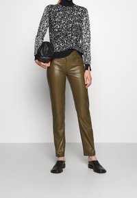 Pull imprimé léopard noir et blanc avec poignets côtelés, pantalon en cuir vert olive, sac noir et chaussures noires sans lacets.