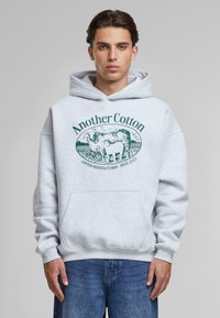 Gray cotton hoodie featuring a front pocket and a green printed logo of a cow with the text “Another Cotton” and “COTTON MANUFACTURER - SINCE 2023.”