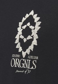 Sort beklædning med et tekstureret sølvlogo af et løvehoved, samt teksten "Studio Atelier ORGNLS sommeren '90" nedenfor.