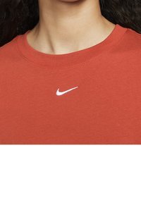 Red cotton t-shirt with a round neckline featuring a small white Nike logo centered on the chest. Smooth texture and short sleeves.
