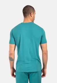 Camiseta atlética de color aguamarina con mangas cortas, escote redondo y una textura suave. Vista desde la parte posterior, mostrando un diseño minimalista.