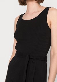Top sin mangas negro con cuello redondo y cinturón de tela a juego en la cintura. La textura es suave y tiene un diseño ajustado.