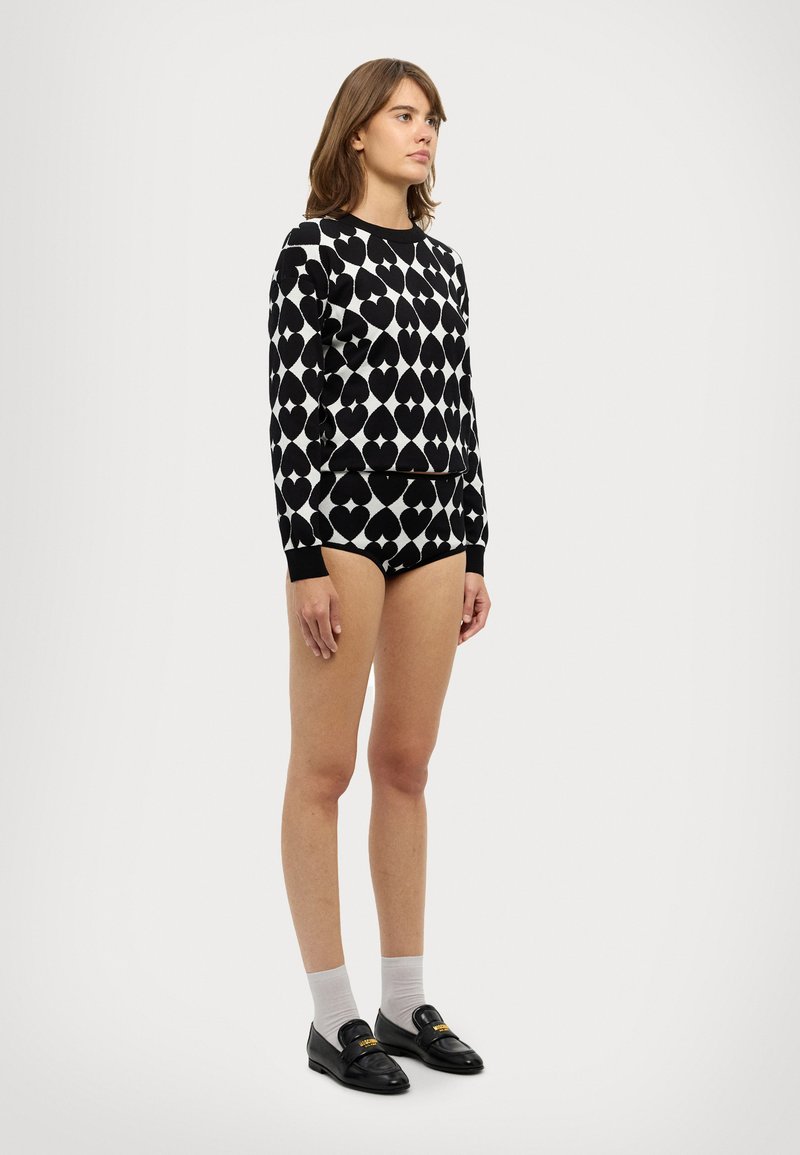 Sweatshirt padrão em preto e branco com motivos de corações, combinado com calções pretos a condizer. Modelo usa mocassins pretos e meias cinzentas.