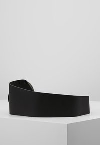 Sort læderbælte med glat overflade, bredt design og cirkulær metalspænde. Simpel og minimalistisk stil, præsenteret på en hvid platform.