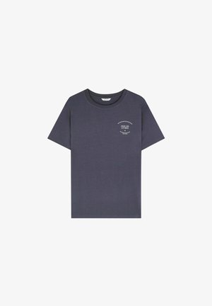 Mørkegrå T-shirt med korte ærmer og lille hvid cirkulær tekstdesign på venstre bryst, der læser "Joie de Livres" og andre sætninger.