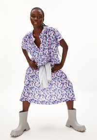 Blumenkleid in Lila, Pink und Weiß mit kurzen Ärmeln und einem Kragen; kombiniert mit hellgrauen Ankle Boots mit einer klobigen Sohle.