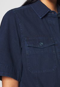 Mörkblå denimskjorta med korta ärmar, utrustad med två bröstfickor med knäppningar, samt en klassisk kragdesign.