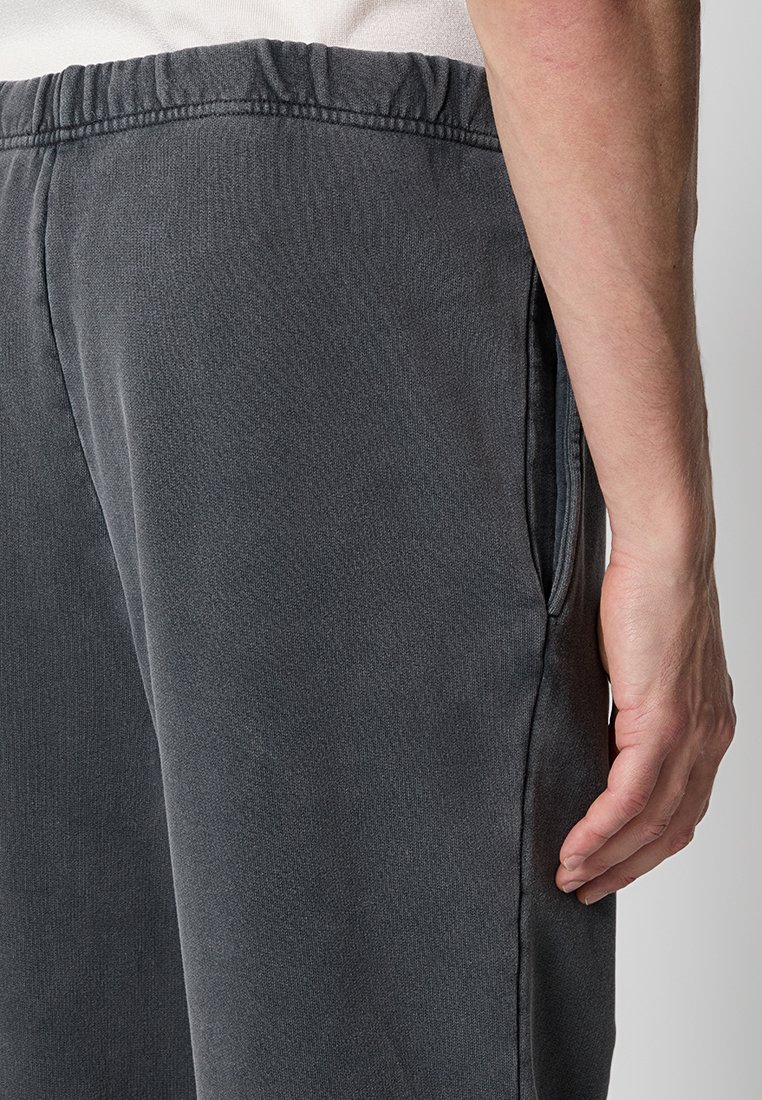 Pantalones de chándal gris oscuro con un acabado texturizado, cinturilla elástica y bolsillos laterales. Mostrando una vista en primer plano del lado derecho.