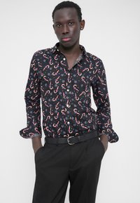 Svart skjorte med knapper, prydet med et candy cane-mønster i rødt og hvitt, og blomsterdetaljer, kombinert med svarte bukser og belte.