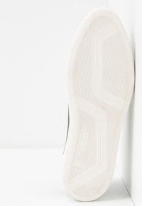 Suela de goma blanca con patrón de espiga; paneles laterales grises; logotipo de la marca grabado en la suela; textura suave; diseño minimalista.