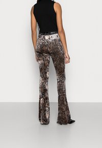 Vapaa-mallinen housut korkean vyötärön ja käärmeennahan kuviolla, jossa on kiiltävä, tekstuurinen kangas ruskean ja mustan sävyissä. Mukava, joustava vyötärö.