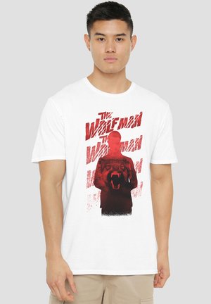 Young man wearing a white T-shirt with red graphic of a growling wolf overlaying a shadowed figure and "The Wolf Man" text.