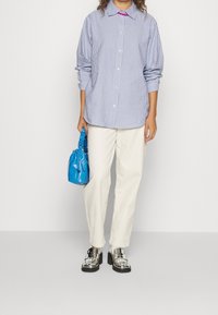 Sininen ja valkoinen raidallinen paita, napitettu, pitkät hihat. Valkoiset kapeat housut. Hopeiset platform-kengät. Sininen teksturoitu käsilaukku kädessä.