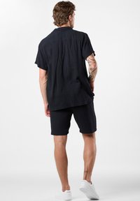 Sort krøllet bomulds skjorte og shorts outfit. Kortærmet skjorte med en afslappet krave, parret med matchende shorts og hvide sneakers.