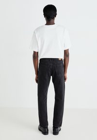 Pantaloni negri din denim cu croială dreaptă, cu talie înaltă, cinci buzunare și detalii minime de cusătură. Asortați cu un tricou alb simplu.