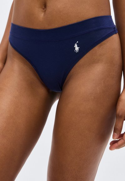 Slip bikini bleu marine avec logo Polo Ralph Lauren blanc porté par une personne à la carnation moyenne foncée, présenté de la taille jusqu'au milieu de la cuisse.