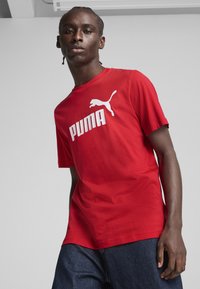 Rotes Baumwoll-T-Shirt mit übergroßem weißen "PUMA"-Logo und springendem Puma-Graphic, kurzen Ärmeln und lockerer Passform.