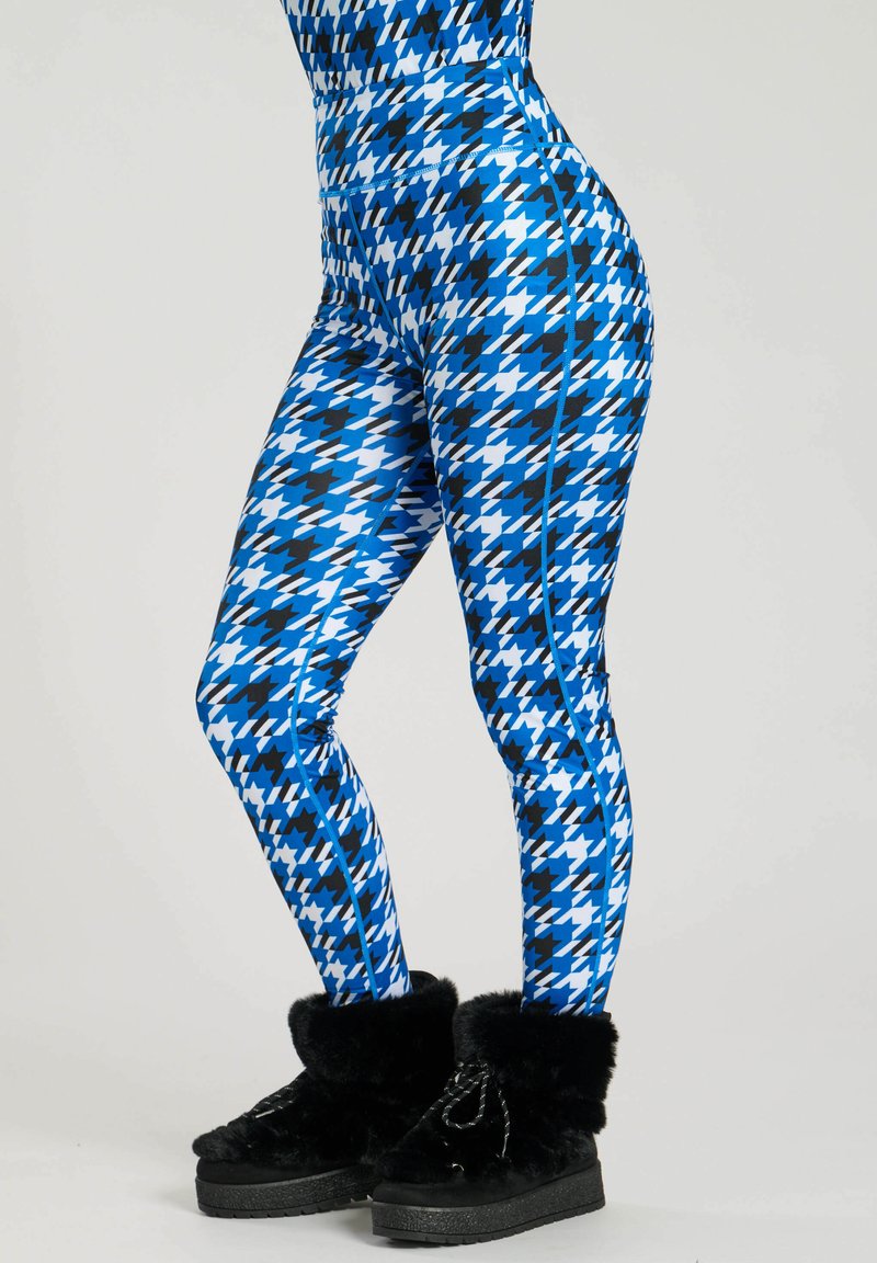 Leggings aderenti con un motivo a quadri houndstooth blu, nero e bianco, con pannelli laterali blu a contrasto, abbinati a stivali neri foderati in pelliccia.