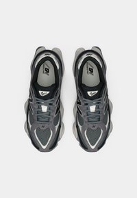 Baskets de sport grises avec une tige en mesh, accents noirs contrastants et une semelle rembourrée. Présente un logo sur la languette et les lacets.