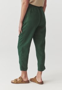 Pantalons légers verts avec une coupe décontractée, une taille élastique et des ourlets roulés. Associés à des sandales à enfiler marron.