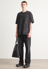 Svart oversized t-skjorte med subtil tekstur, kombinert med mørkejeans. Holder en svart tote-bag og har på seg kraftige svarte skinnsko.