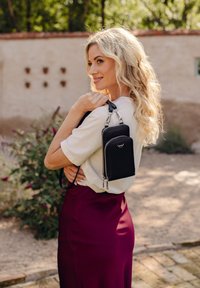 Black faux leather crossbody bag with zippered compartments, silver hardware, and adjustable strap, held against a light-colored background.