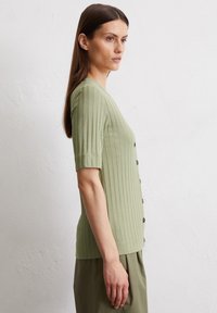 Hellgrünes, geripptes Strickoberteil mit kurzen Ärmeln und V-Ausschnitt, ausgestattet mit einer Reihe dunkler Knöpfe auf der Vorderseite. Glatte Textur mit minimalistischem Design.