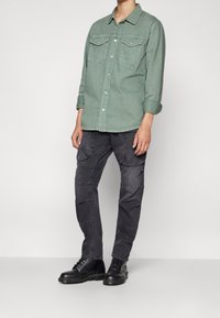 Grön denimskjorta med knäppning och två bröstfickor, i kombination med texturerade svarta jeans och svarta snörboots.