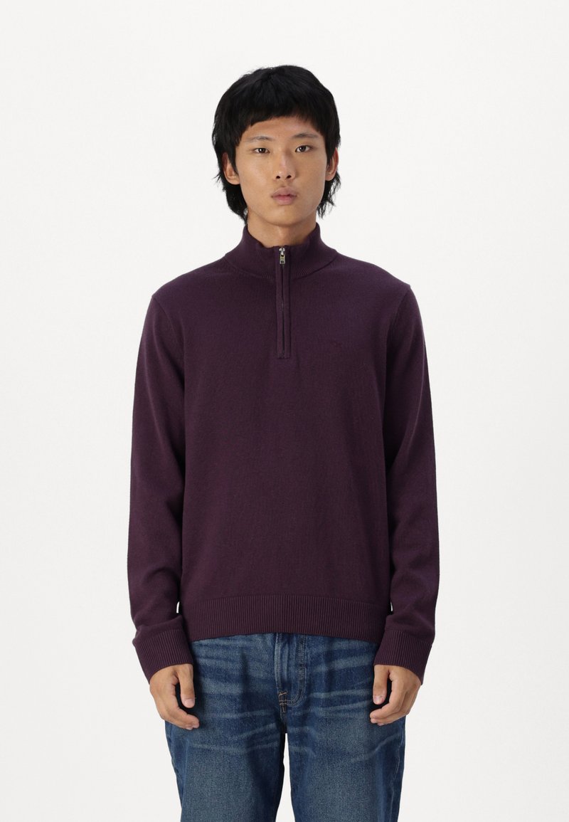 Maglione con collo zip viola realizzato in tessuto a maglia, con polsini e orlo a coste, abbinato a jeans in denim blu. Design semplice e moderno.