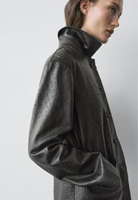 Zwarte leren jas met een gestructureerd, reliëf design. Voorzien van een hoge kraag, knoopsluitingen en een losse pasvorm.