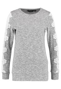 Grå sweatshirt med långa ärmar som har vita spetsblommor längs ärmarna. Rund halsringning och ribbade mudd. Mjuk och bekväm tygtextur.