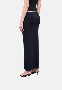 Falda maxi negra de canalé con cintura ajustada y silueta recta, combinada con sandalias de tacón negro con tiras. Textura suave.