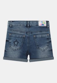 Shorts de mezclilla con dobladillos enrollados, dos bolsillos traseros, un bordado de estrella en el bolsillo izquierdo y una etiqueta de marca colorida en la cinturilla.