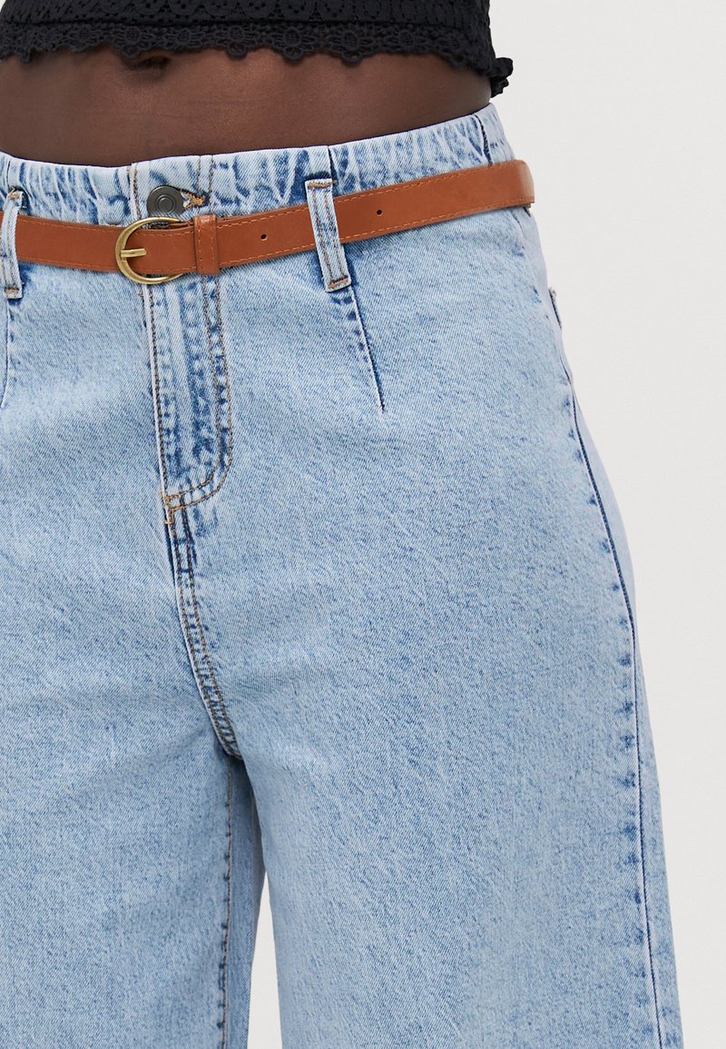 I jeans in denim blu chiaro presentano un'alta vita, una gamba dritta e una cintura in pelle tan con una fibbia dorata tonda.