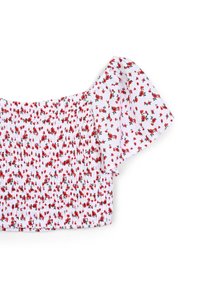 Blusa bianca con motivo floreale rosso, dettagli con arricciatura elastica, maniche corte a sbuffo, tessuto morbido e scollo ondulato.