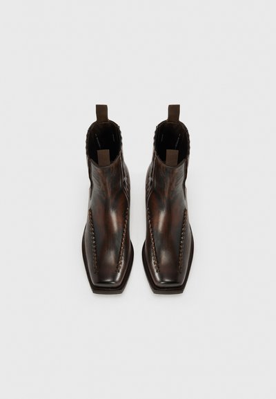 Botas de cuero marrón hasta el tobillo con punta afilada, detalles de costura a lo largo de los lados y lengüetas en los tobillos. Textura suave.