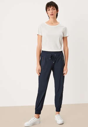 Marine joggingbroek met ritszakken aan de zijkant en een trekkoord in de taille, gecombineerd met een witte t-shirt met ronde hals. Witte sneakers maken de look compleet.