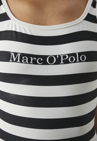 Maillot de bain à rayures noir et blanc avec un décolleté en forme de scoop, avec "Marc O'Polo" imprimé au centre et "EST. À STOCKHOLM" en dessous.
