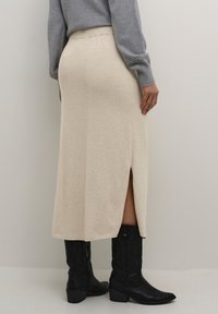 Jupe midi en tricot côtelé beige avec fente latérale, portée avec un pull gris et des bottes de cowboy noires. Dotée d'une taille élastique et de détails texturés.