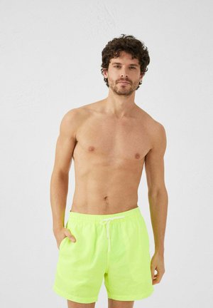 Bañador amarillo brillante con cinturilla elástica, detalle de cordón y bolsillos laterales. Tejido suave y ligero.